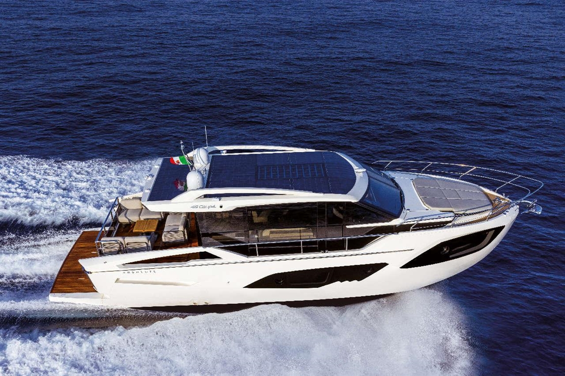 Luxury yacht cruising through waves, featuring a solar panel on the roof and a sleek white design against a blue ocean.